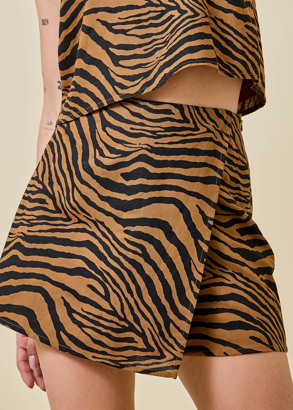 A lovely lady models our Tiger, Fierce & Fabulous Wrap Skort in a soft, flowy fabric that’s as comfortable as it is eye-catching. The brown and black tiger stripe pattern adds a bold touch, while the matching top creates a pulled-together look. This skort sits just right at the waist with an easy wrap design for flattering fit and movement, all styled against a warm beige backdrop. Elle Boutique, Zachary, LA.