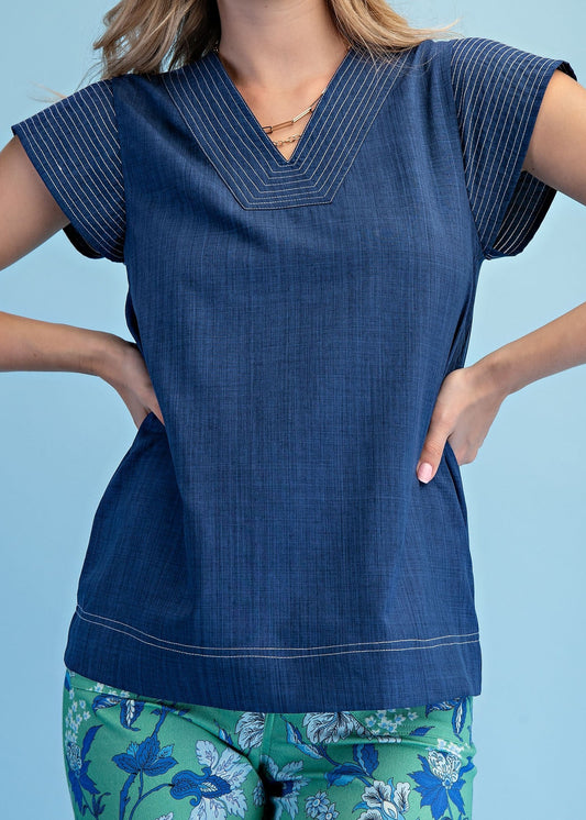 A lady shows off our soft cotton Blue Haven Blouse with a breezy V-neck and fine stitching, plus green floral pants. Elle Boutique, Zachary, LA.