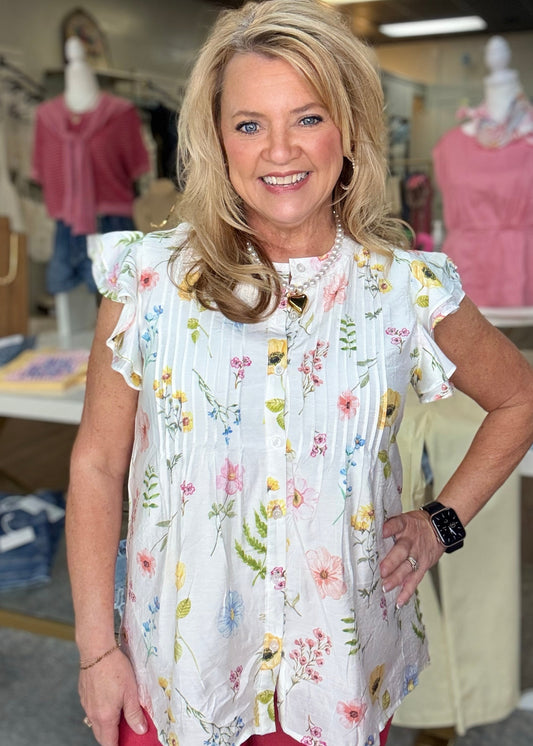 A smiling blonde models our soft cotton-blend Petal Charm Blouse with ruffle sleeves and a sweet floral print at Elle Boutique, Zachary, LA.