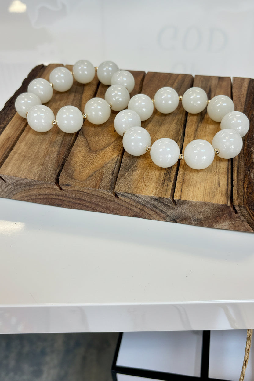 Charming stretch bracelet with creamy ivory beads and dainty gold spacers, set on a rustic tray. Elle Boutique, Zachary, LA.