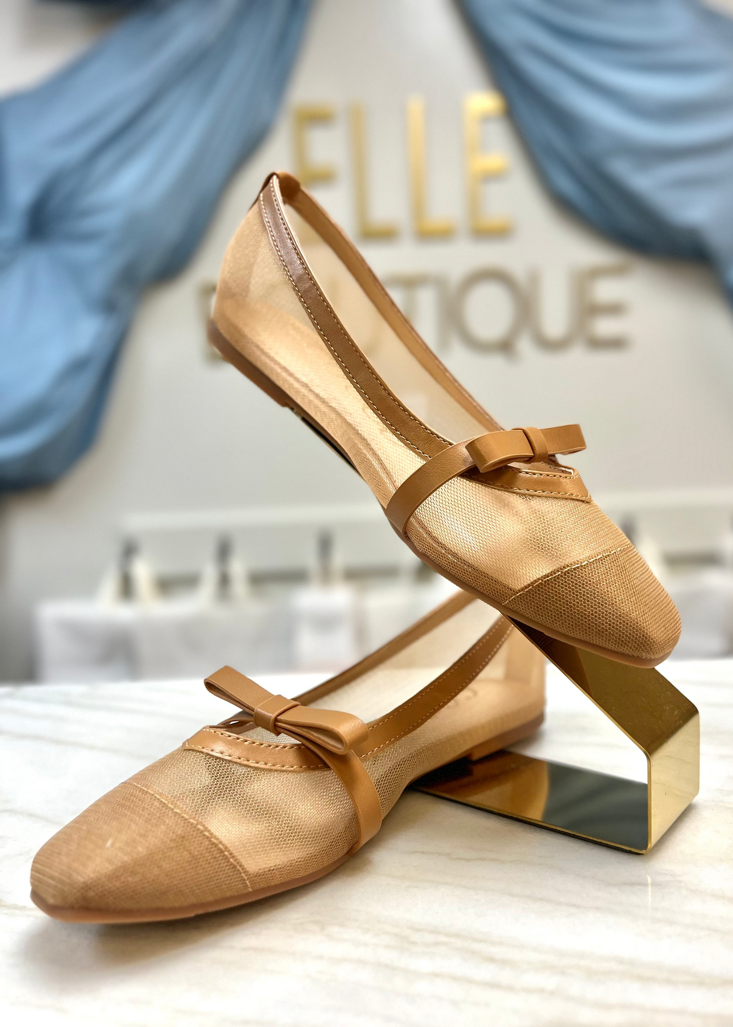 Sweet camel ballet flats with comfy fit and brown leather bows, styled on marble and gold at Elle Boutique, Zachary, LA.