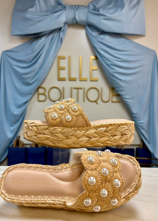 Chic raffia platform sandals adorned with pearl beads and soft natural straps, set by a blue ribbon and gold sign. Elle Boutique, Zachary, LA.