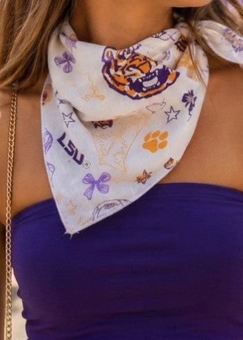 A gal in a soft, comfy purple top has the LSU Tigers Game Day Bandana Scarf tied sweetly around her neck. The scarf shows off playful tiger prints, golden paw prints, and pretty floral touches—a blend of school spirit and Southern charm. Lightweight, with a relaxed fit for easy all-day wear and pops of LSU golds and purples. Elle Boutique, Zachary, LA.