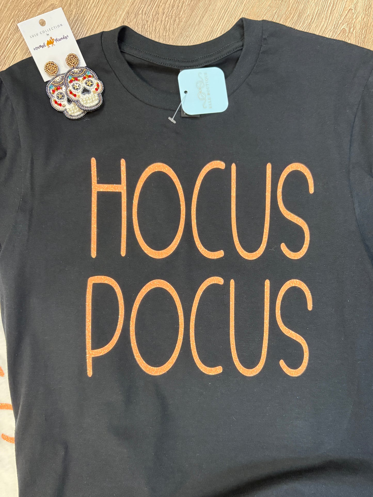 Add a dash of whimsy to your wardrobe with this comfy, soft cotton black tee, highlighted by bold orange “HOCUS POCUS” lettering across the front. The relaxed fit makes it perfect for layering or tucking into your favorite jeans. Up top, you’ll spot a precious card featuring beaded skull earrings that add just the right amount of Southern charm and playful spirit. All from Elle Boutique, Zachary, LA.