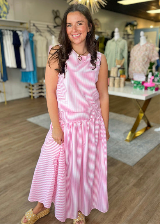 A woman beams in a pink striped midi set—soft cotton, flowy fit, sweet tie waist—paired with tan sandals. Elle Boutique, Zachary, LA.