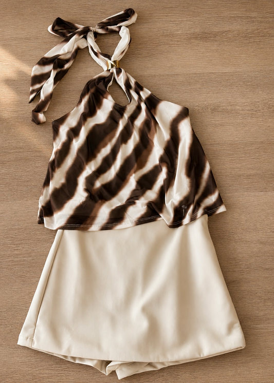 This darling outfit features a soft, brown and white tie-dye halter top with a flattering keyhole neckline, perfect for warm Southern days. It’s paired sweetly with the Sweet Talk Cream Pleather Skort, offering an easy fit and fun faux leather texture in a creamy hue. Both pieces are showcased against rustic wood, creating that true Southern charm. Elle Boutique, Zachary, LA.