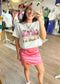 A cheerful gal snaps a mirror selfie in a pink satin mini skirt and soft flamingo tee, surrounded by cute finds. Elle Boutique, Zachary, LA.