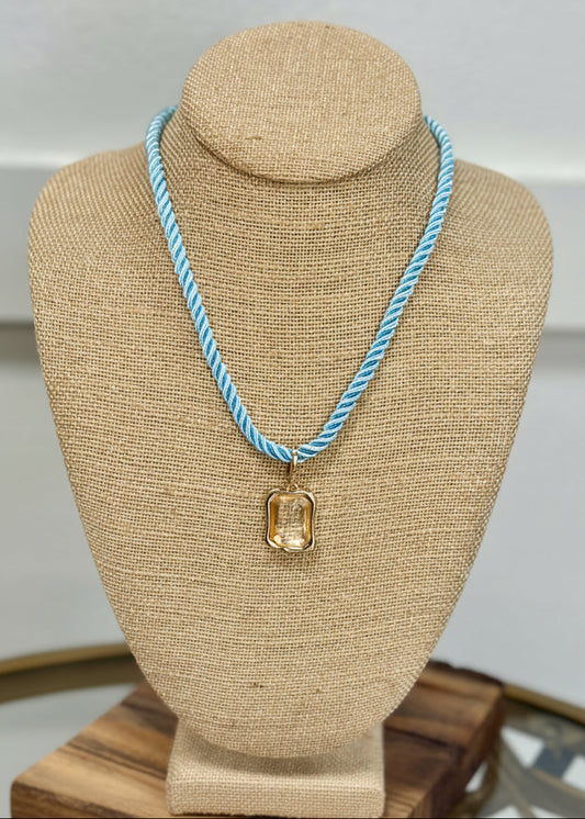 Shimmery gold charm necklace with a clear gem, light blue rope, perfect coastal accent. Elle Boutique, Zachary, LA.