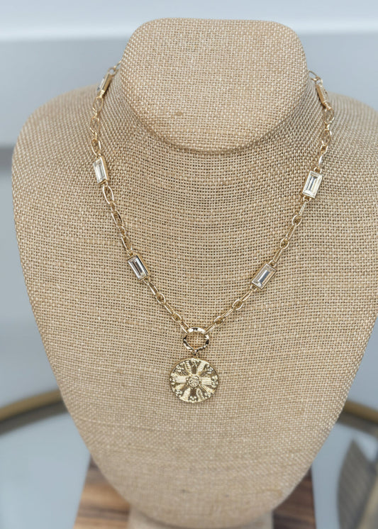 The Gold Crystal Medallion Necklace shimmers with gold and crystal touches, featuring a classic round pendant. Elle Boutique, Zachary, LA.