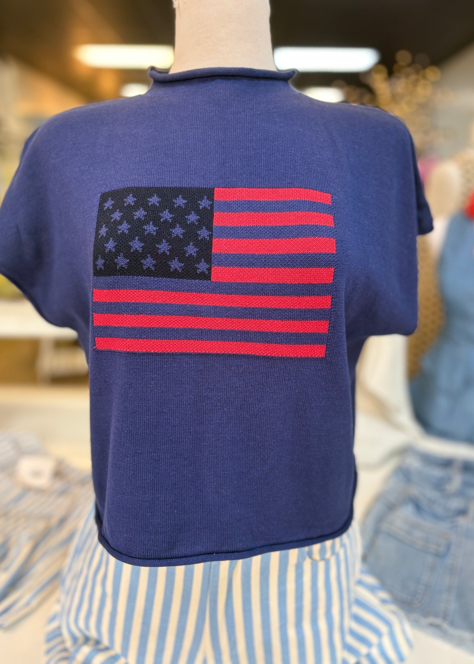 A cozy, lightweight USA flag sweater with navy stars and cherry red stripes pairs with striped high-rise pants; denim shorts peek behind. Elle Boutique, Zachary, LA.