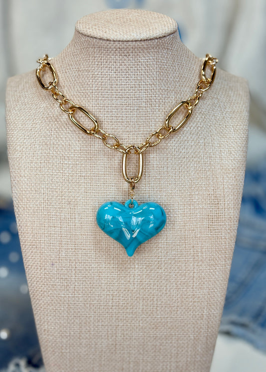 A darling gold chain with bold oval links and a glossy turquoise heart charm, shown on soft beige. Elle Boutique, Zachary, LA.