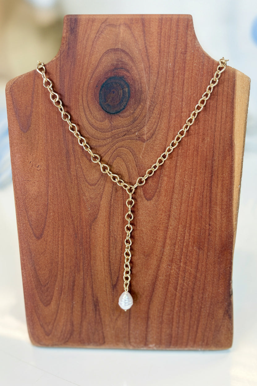 Sweet Southern charm shines in this gold lariat chain necklace with a dainty pearl drop, shown on wood. Elle Boutique, Zachary, LA.
