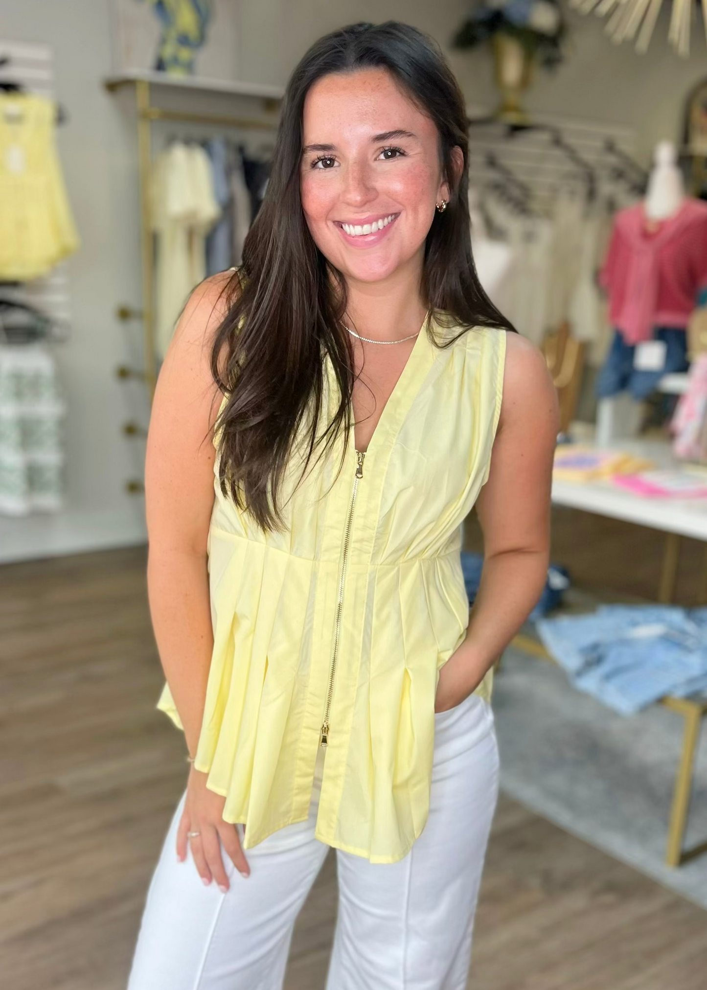 A cheerful woman in a sunny yellow peplum zip top and white pants stands inside Elle Boutique, Zachary, LA.