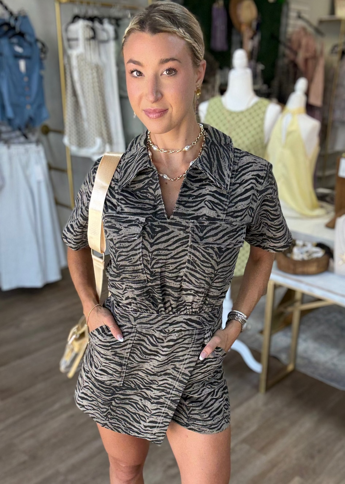 A lovely gal is pictured in the “Roar About It Wrap Front Romper,” showing off its breezy short sleeves and sassy tiger print. This playful piece features a comfy, lightweight fabric with a flattering wrap front, soft elastic waist for an easy fit, and convenient side pockets. The warm tan and black hues make it perfect for mixing wild spirit with Southern charm. She stands inside among sweet clothing displays and stylish mannequins—captured right here at Elle Boutique, Zachary, LA.