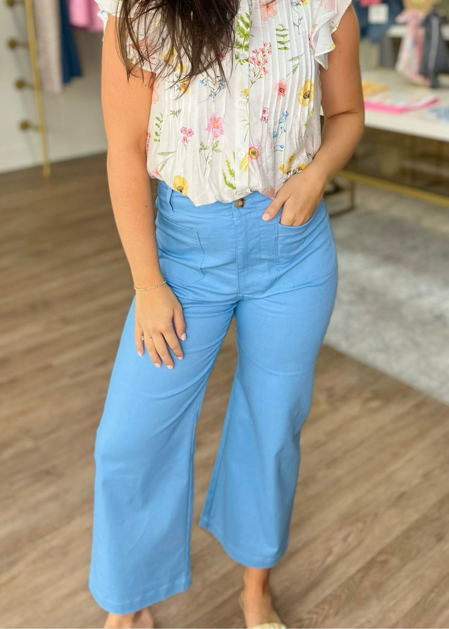 A lady models soft cotton sky blue high-rise wide leg pants and a darling white floral blouse. Elle Boutique, Zachary, LA.