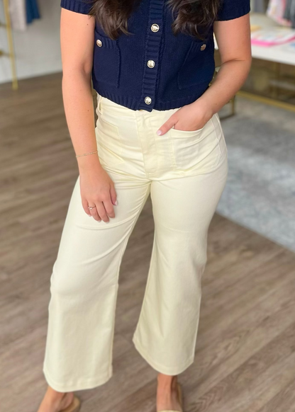 A lady in breezy, lemon-yellow wide leg pants and a navy top with gold buttons stands on wood floors. Elle Boutique, Zachary, LA.