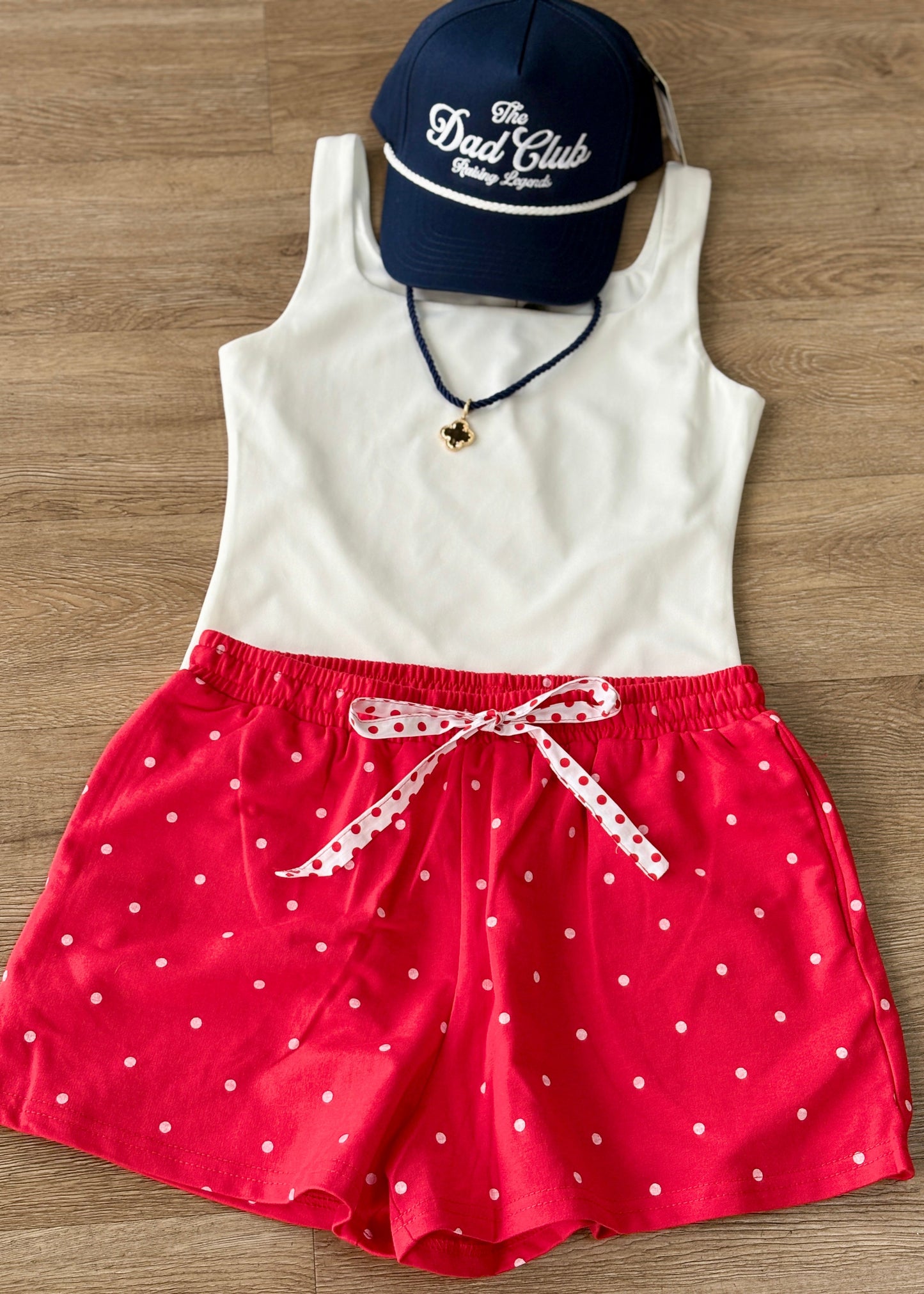 Laid-back charm: soft white tank, comfy polka dot shorts with a ribbon tie, navy Dad Club cap, and a dainty pendant necklace. Elle Boutique, Zachary, LA.
