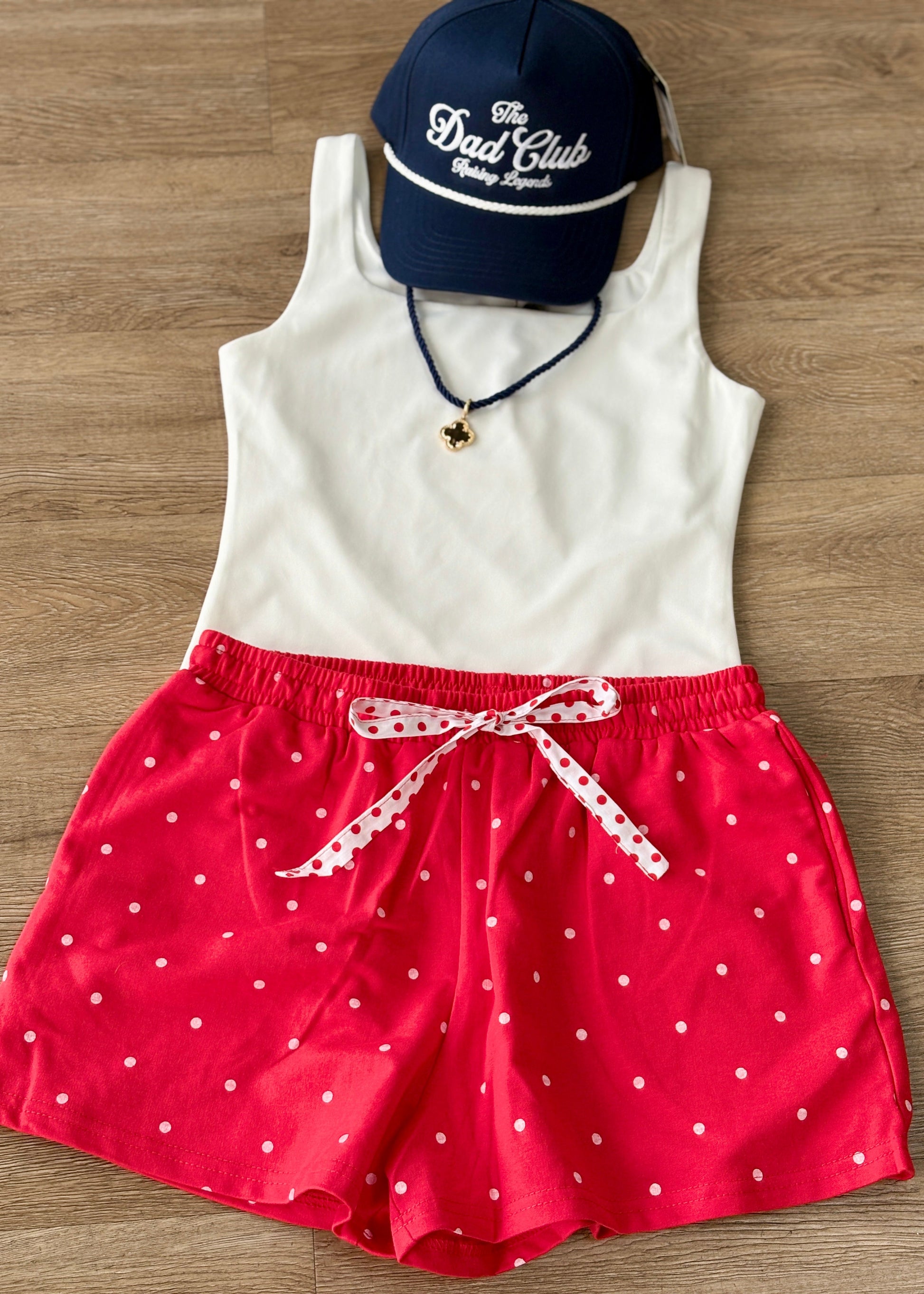 Laid-back charm: soft white tank, comfy polka dot shorts with a ribbon tie, navy Dad Club cap, and a dainty pendant necklace. Elle Boutique, Zachary, LA.
