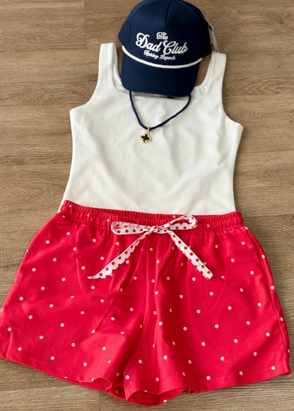 Laid-back charm: soft white tank, comfy polka dot shorts with a ribbon tie, navy Dad Club cap, and a dainty pendant necklace. Elle Boutique, Zachary, LA.