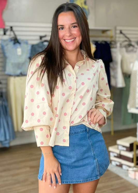 A smiling woman in a breezy polka dot blouse and comfy denim skirt awaits inside our cozy shop. Elle Boutique, Zachary, LA.