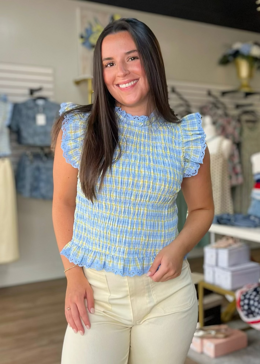 A smiling woman in a soft cotton blue and yellow plaid smocked blouse, comfy cream pants. Elle Boutique, Zachary, LA.