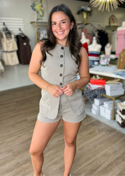 A smiling woman models the navy pinstripe Downtown Darling Vest Set—soft, tailored fit with chic buttons and pockets. Elle Boutique, Zachary, LA.