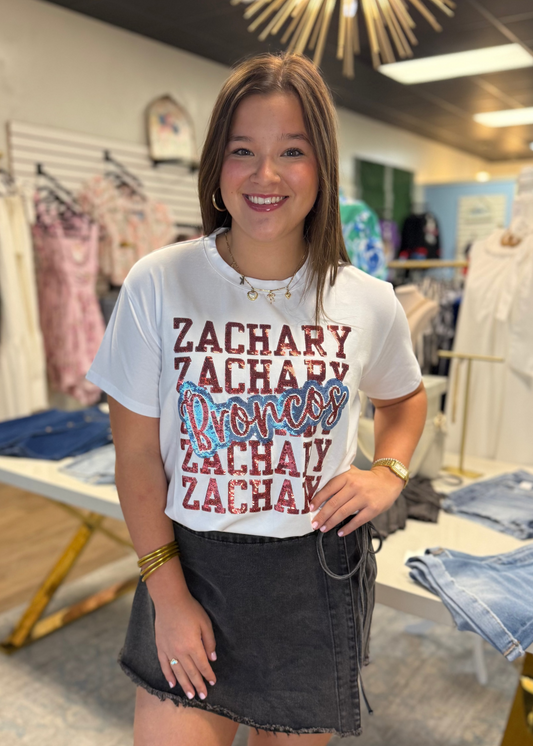 A cheerful gal sports a soft cotton white Zachary Broncos sequin tee and fitted dark denim skirt, boutique charm all around. Elle Boutique, Zachary, LA.