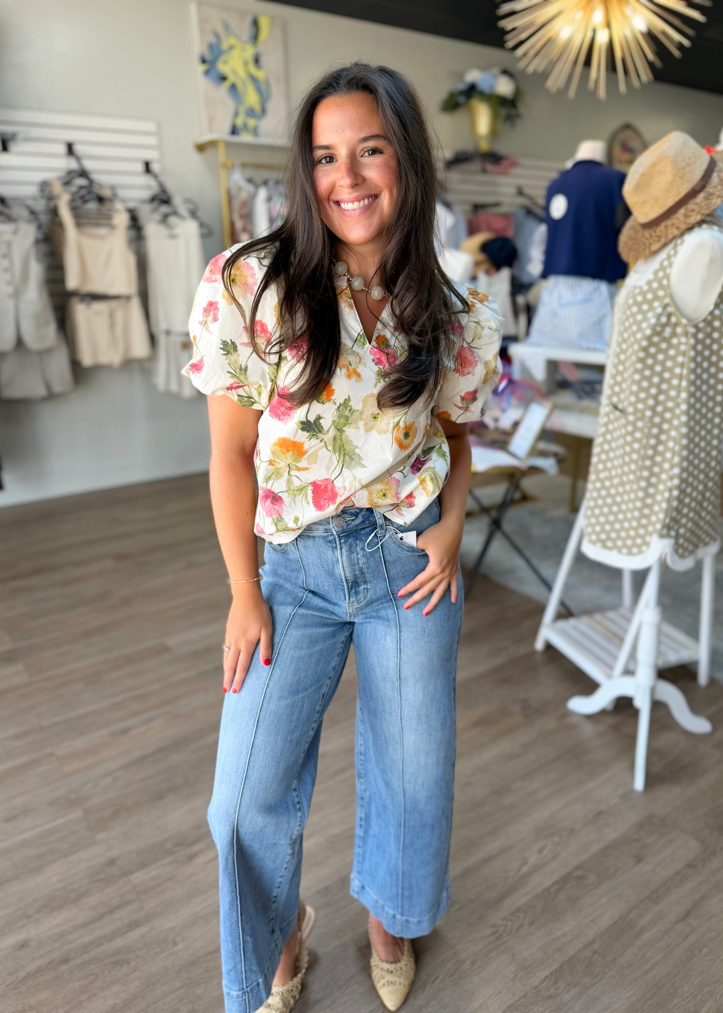 A woman smiles in a soft floral cotton top and easy-fit blue jeans, standing among sweet Southern styles at Elle Boutique, Zachary, LA.