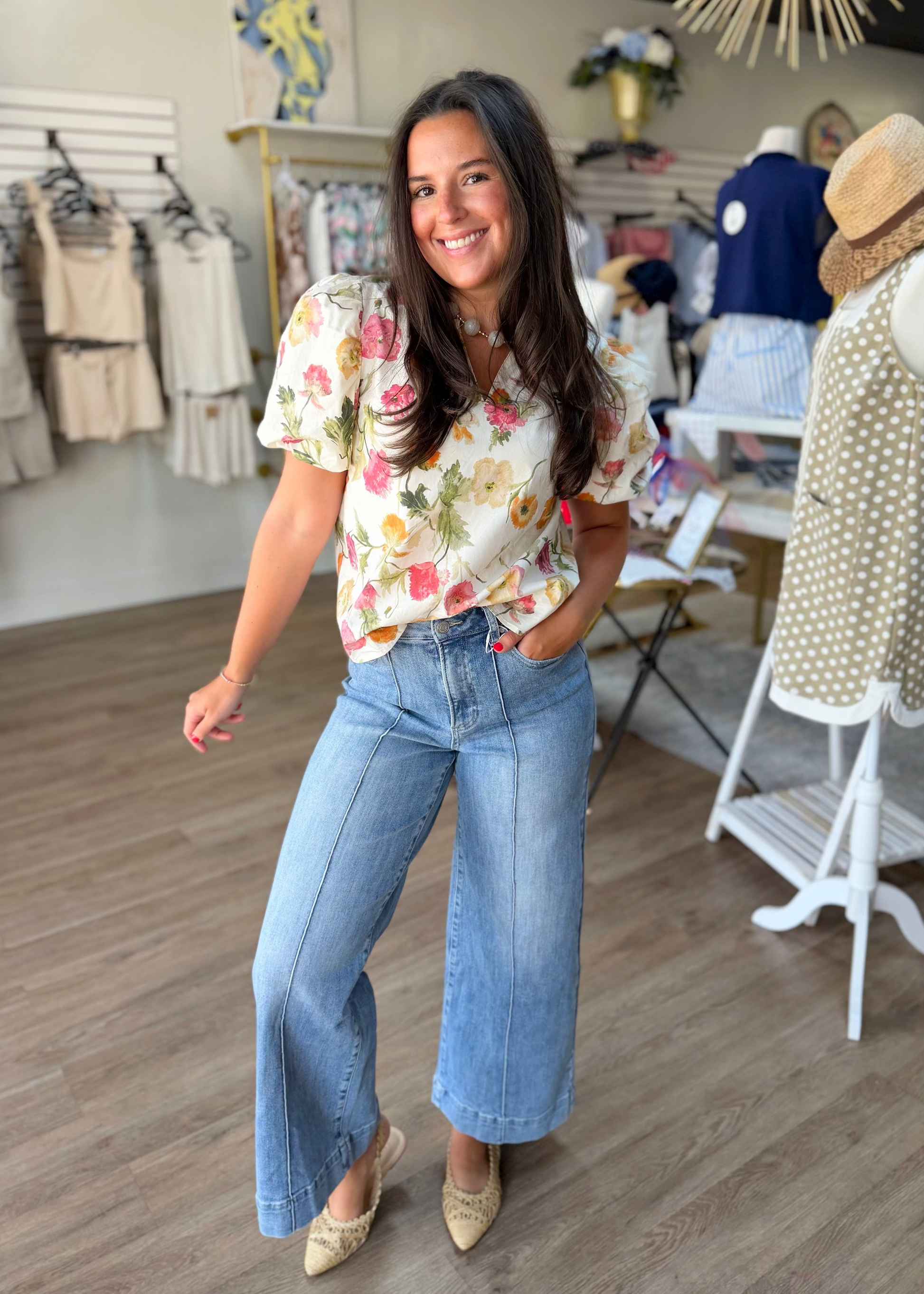 A cheerful woman in a flowy floral cotton blouse and comfy light wash jeans with woven flats, shopping Elle Boutique, Zachary, LA.