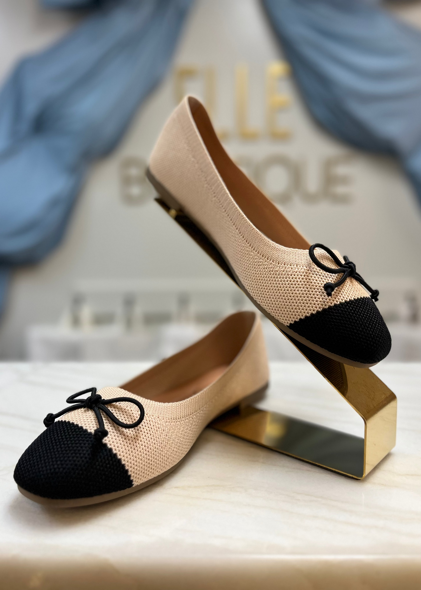 Sweet beige knit ballet flats with a square toe, black cap, and bow—cozy fit and classic charm. Elle Boutique, Zachary, LA.