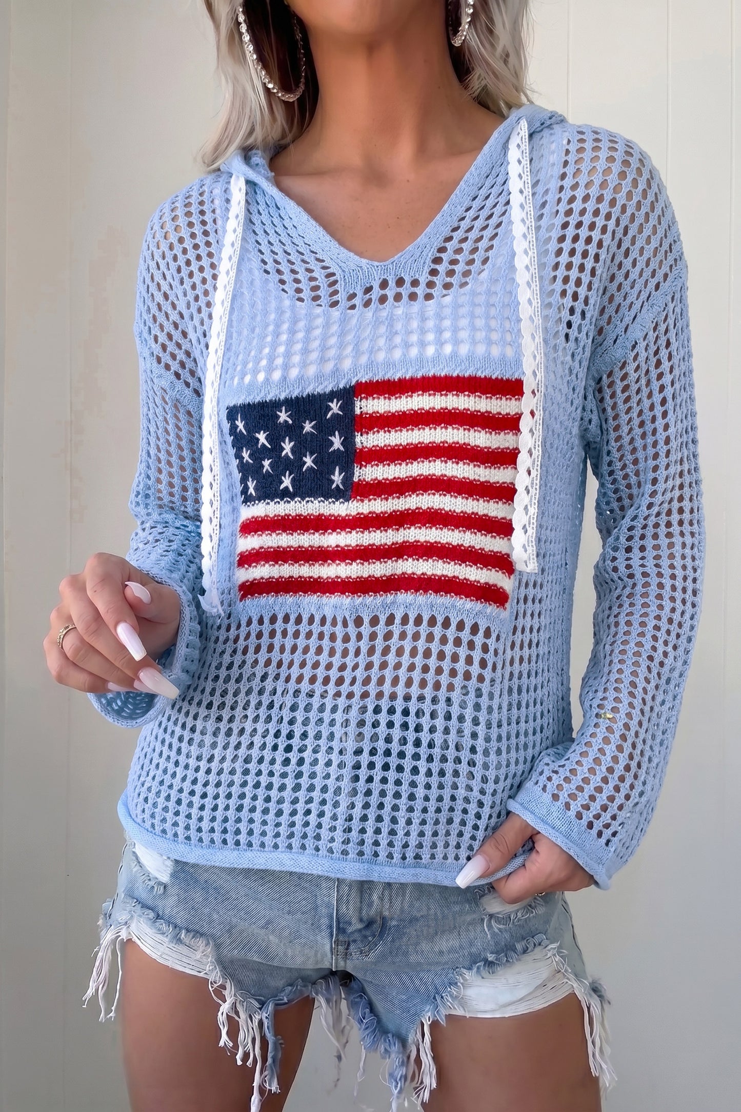 A gal rocks our breezy blue crochet knit flag hoodie with a comfy fit and cute star patches, paired with denim shorts. Elle Boutique, Zachary, LA.